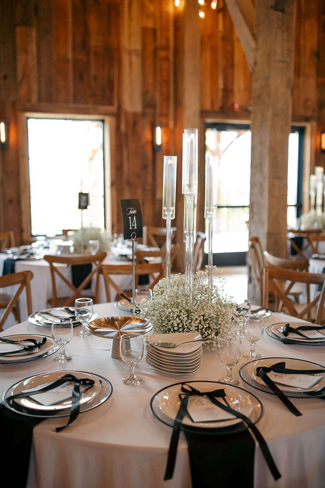 Rustic banquet table set with black plates and glass centerpieces in a wood-beamed dining room