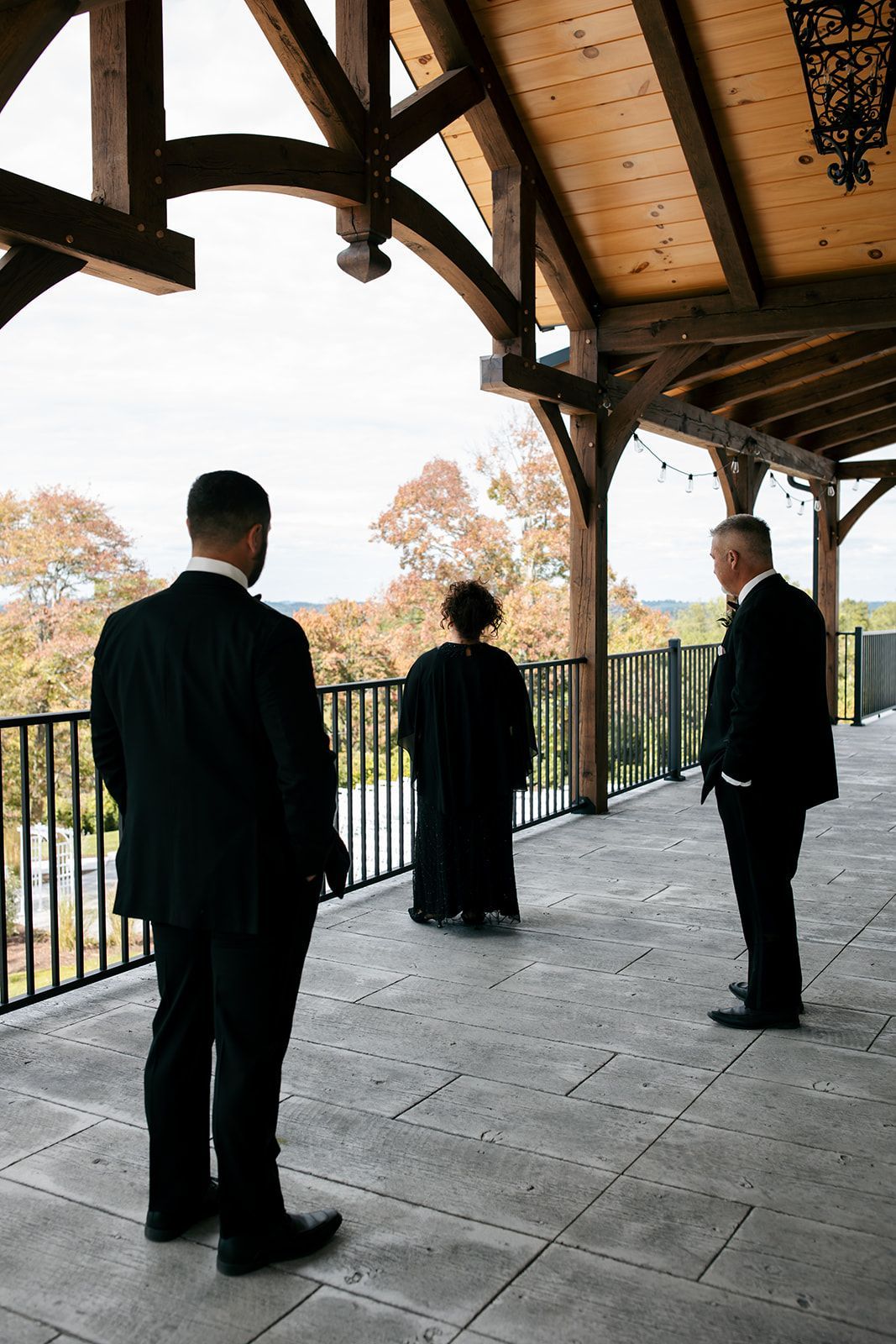 Three people standing on a wooden balcony overlooking autumn trees