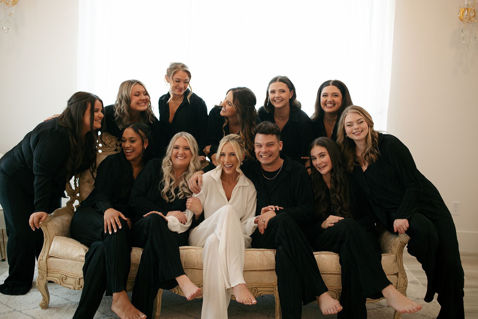 Group of people posing on a couch in formal black and white outfits, with one woman in white at center