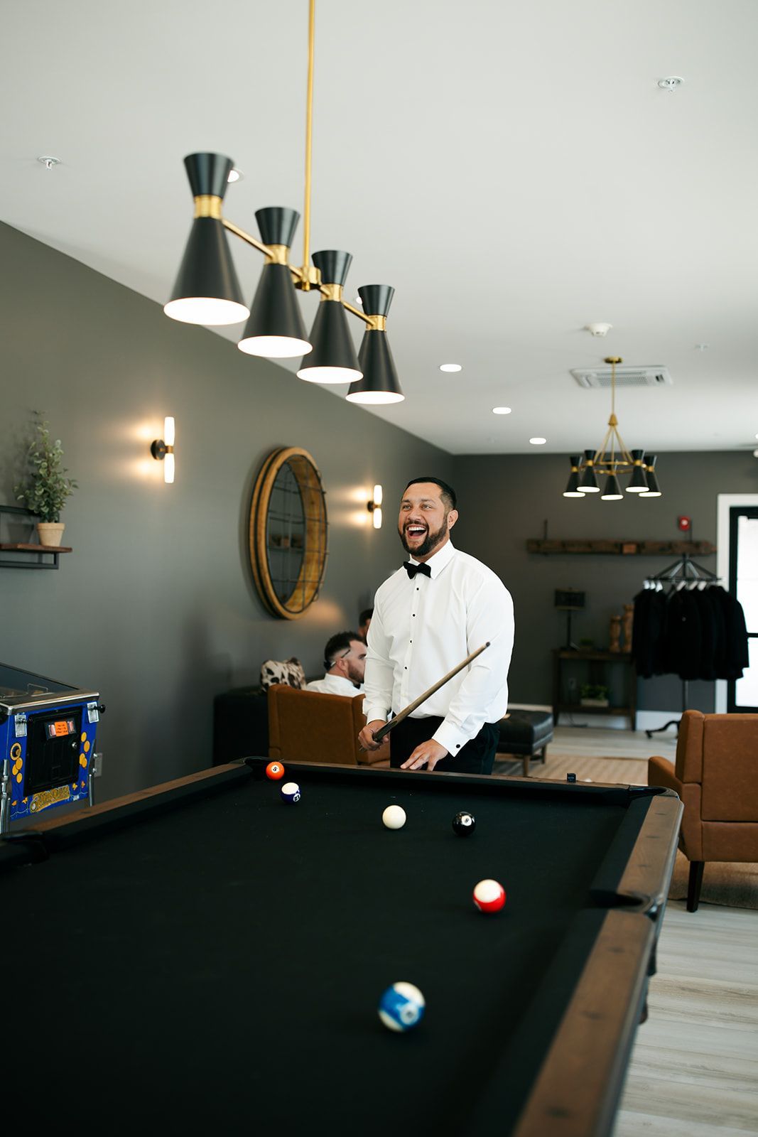 Man standing beside a pool table in a modern billiards room with hanging lights and wall art