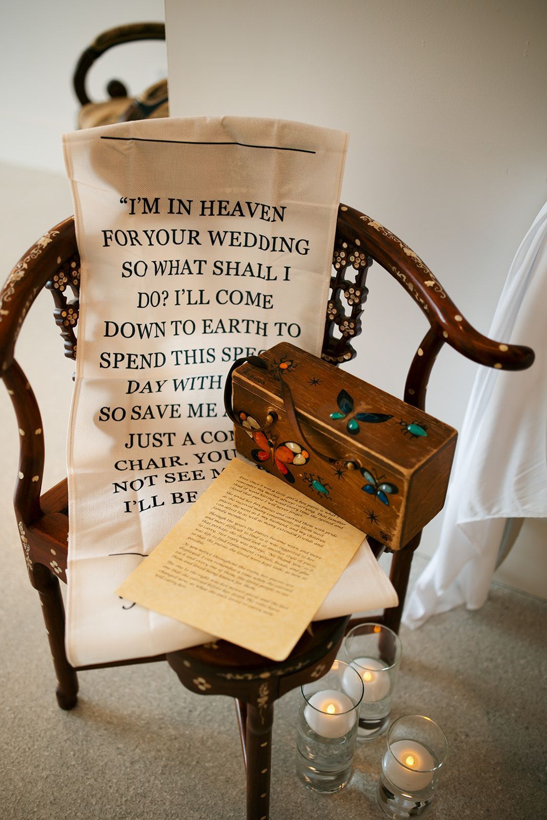 Vintage chair with embroidered sampler, wooden chest, folded letter, and lit candles in a soft-lit room
