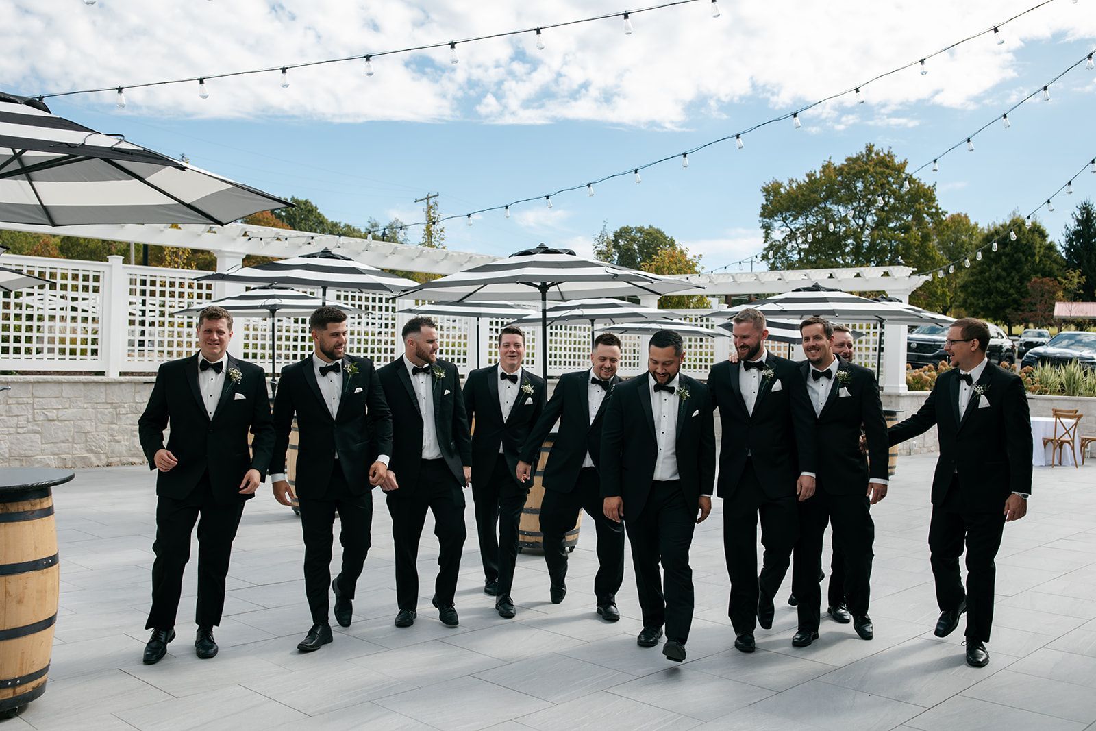 Group of men in black suits walking outdoors at a garden event under string lights