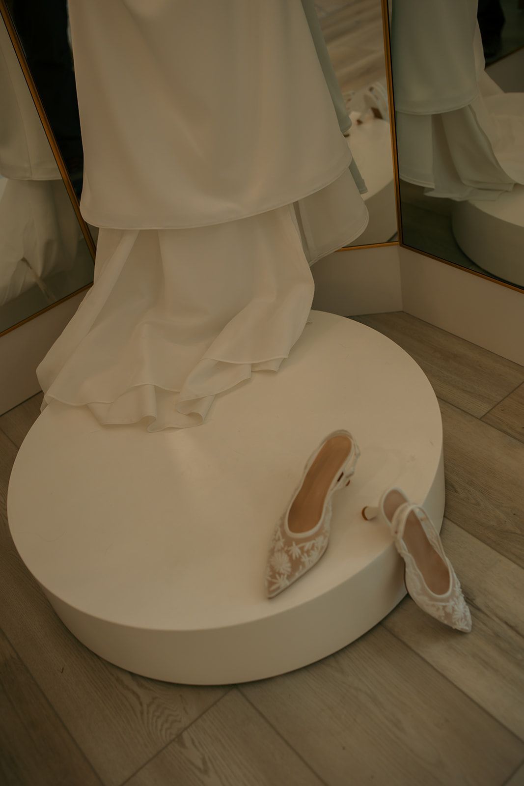 White dress and patterned heels displayed on a round pedestal in a boutique mirror setting
