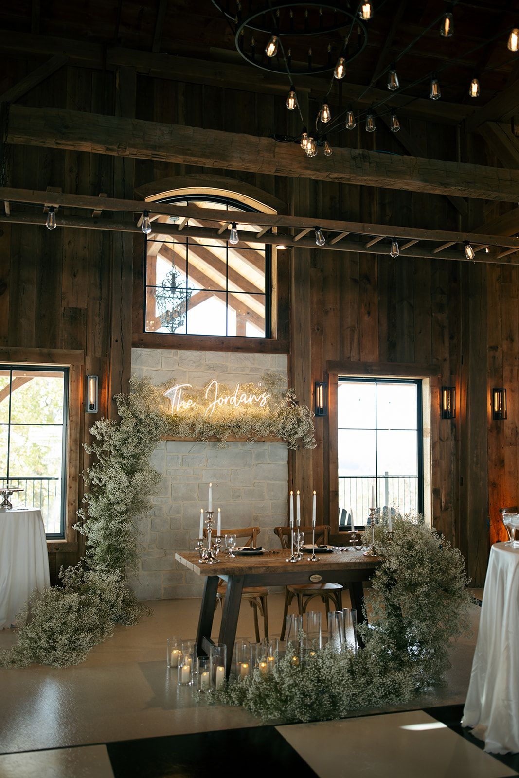 Rustic barn wedding reception setup with floral arch, table, and string lights