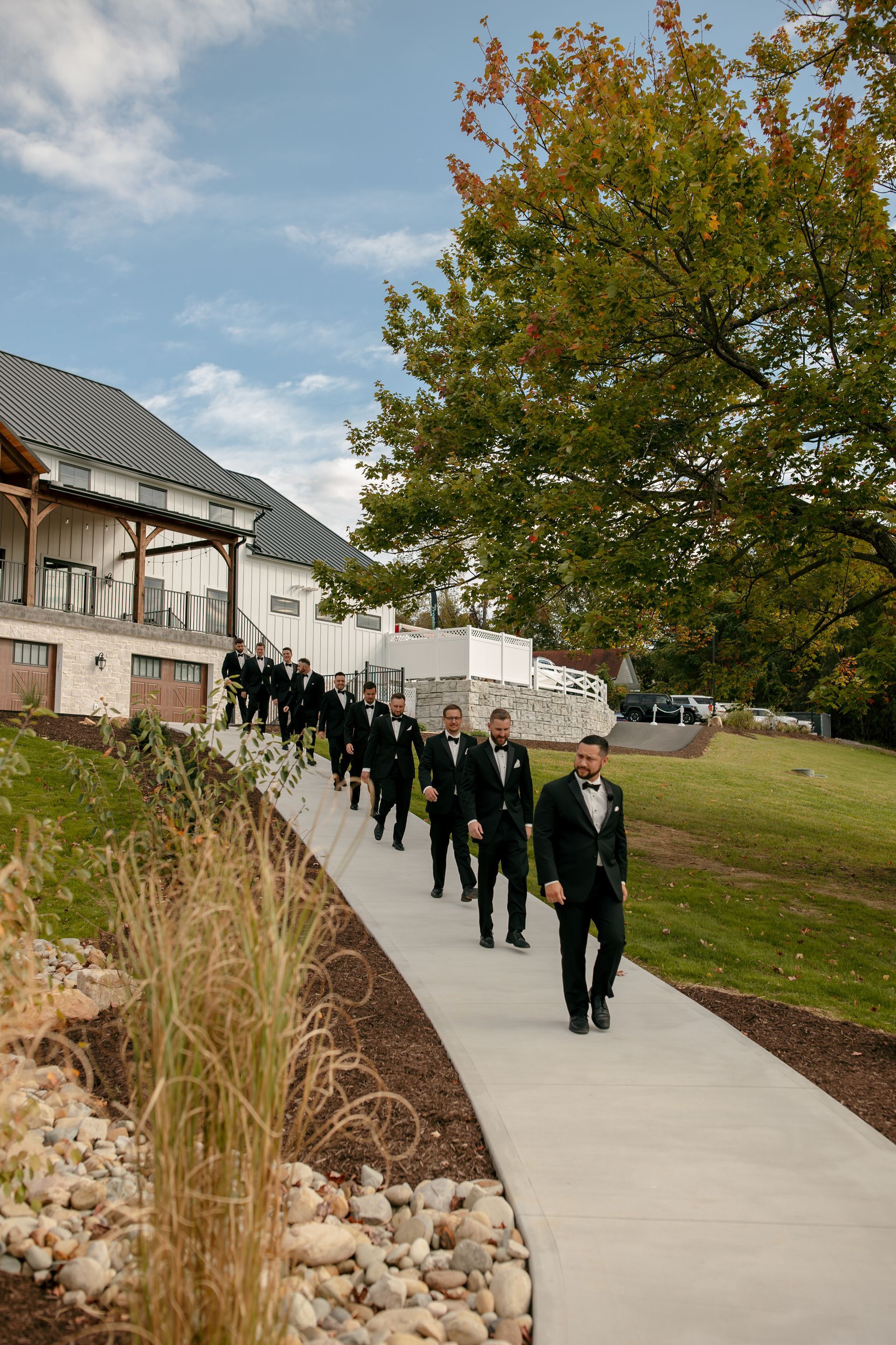 People in dark uniforms walking in a line on a sidewalk beside a building and trees