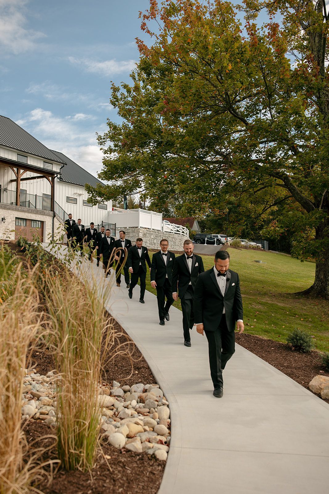 People in black suits walking along a curved path beside a building and autumn trees