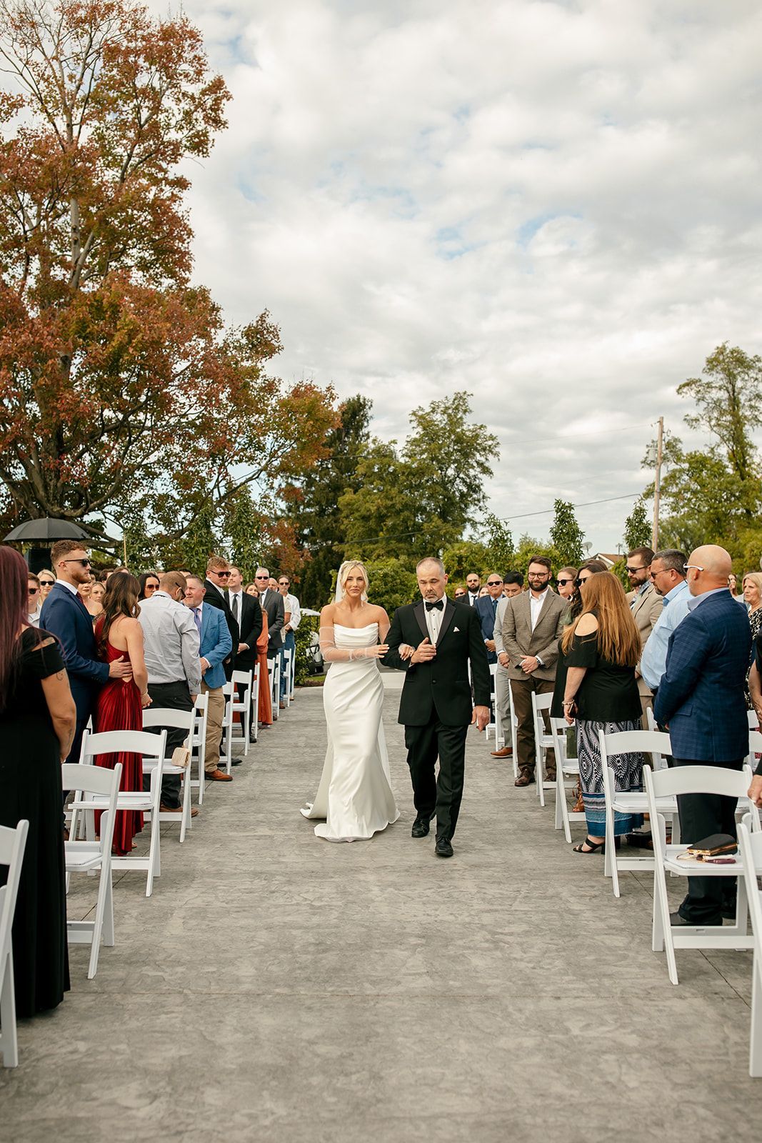 Bride and groom walking down outdoor aisle between seated guests at a wedding ceremony