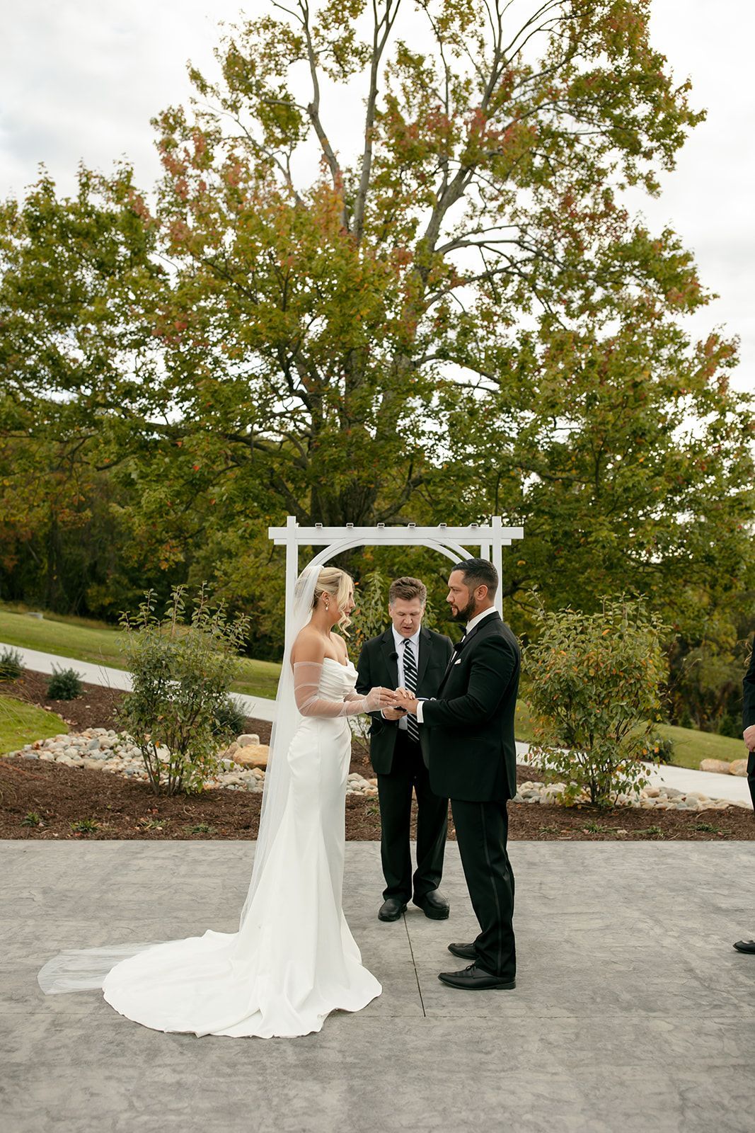 Bride and groom exchanging vows under an arbor outdoors with an officiant behind them