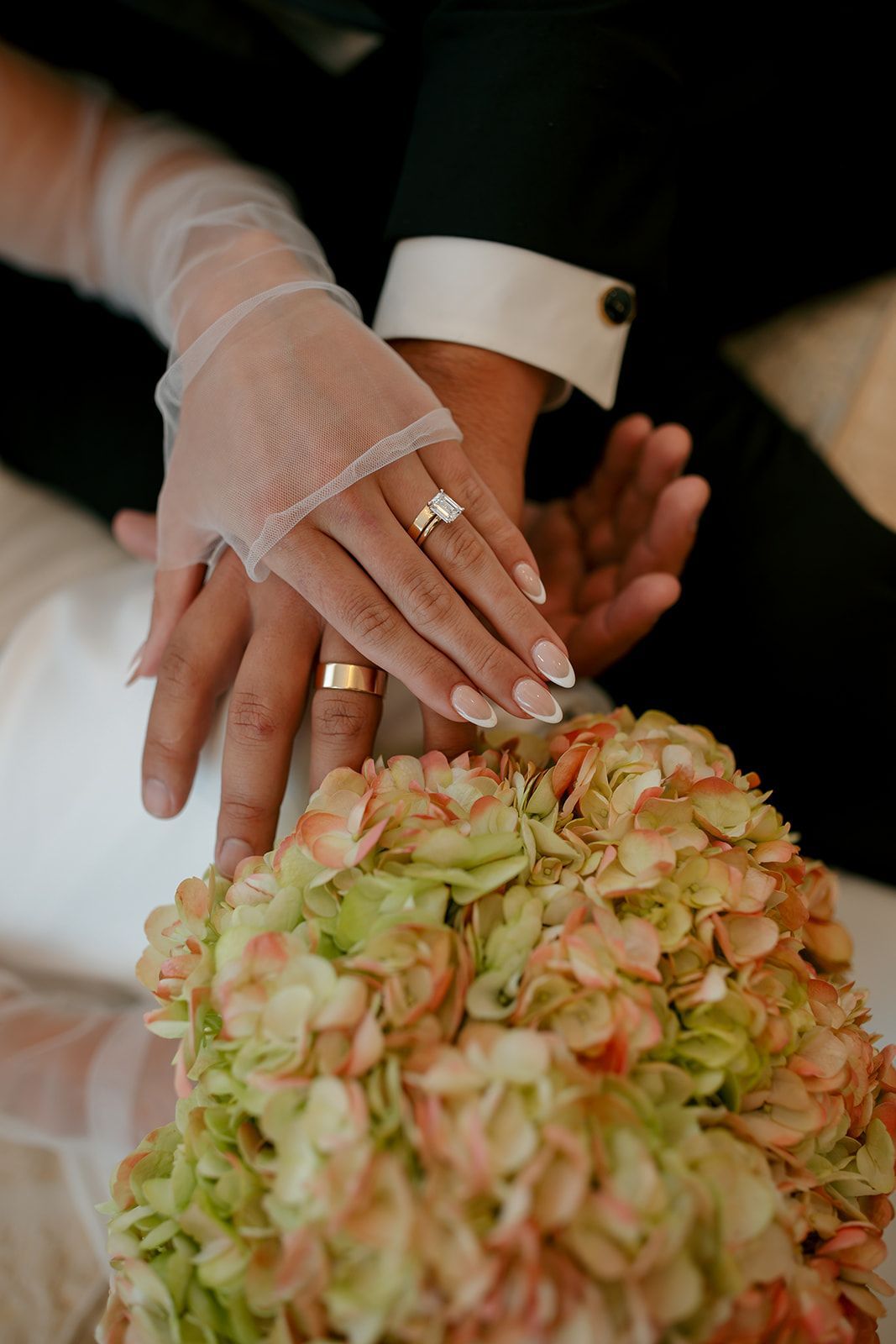 Bride and groom’s hands on a bouquet, showing wedding rings and lace gloves