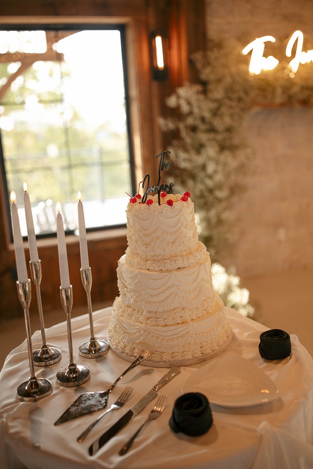 Elegant white tiered cake with candles and tableware on a decorated table by a window