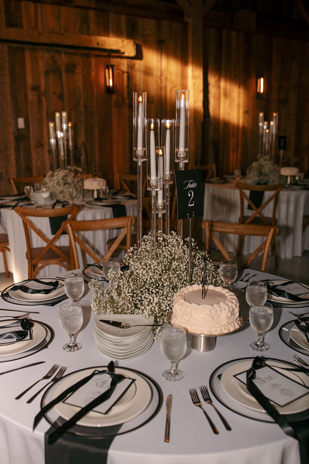 Elegant candlelit banquet table with white tablecloth, black-and-white place settings, and silver candelabra centerpieces