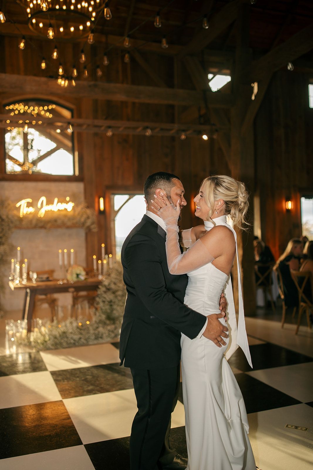 Couple embracing at a candlelit wedding reception in a rustic venue, with black-and-white checkered floor.