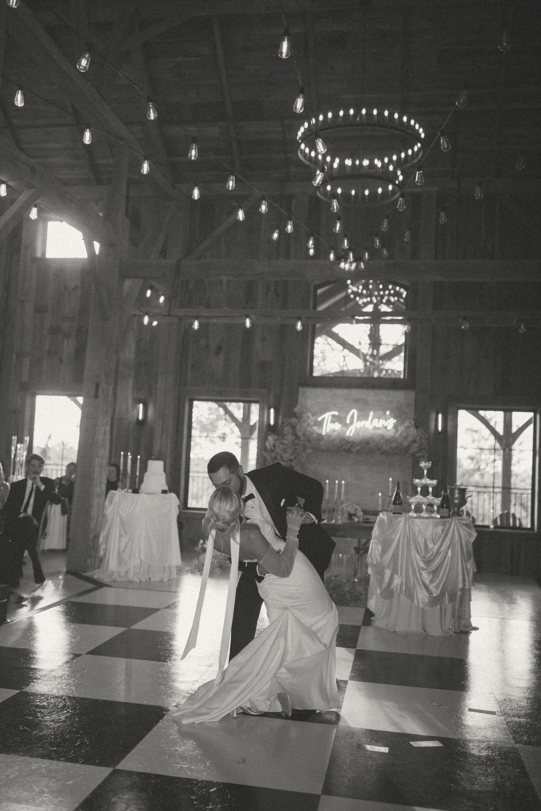 Two people dancing in a dimly lit hall with chandeliers and checkered floor tiles.