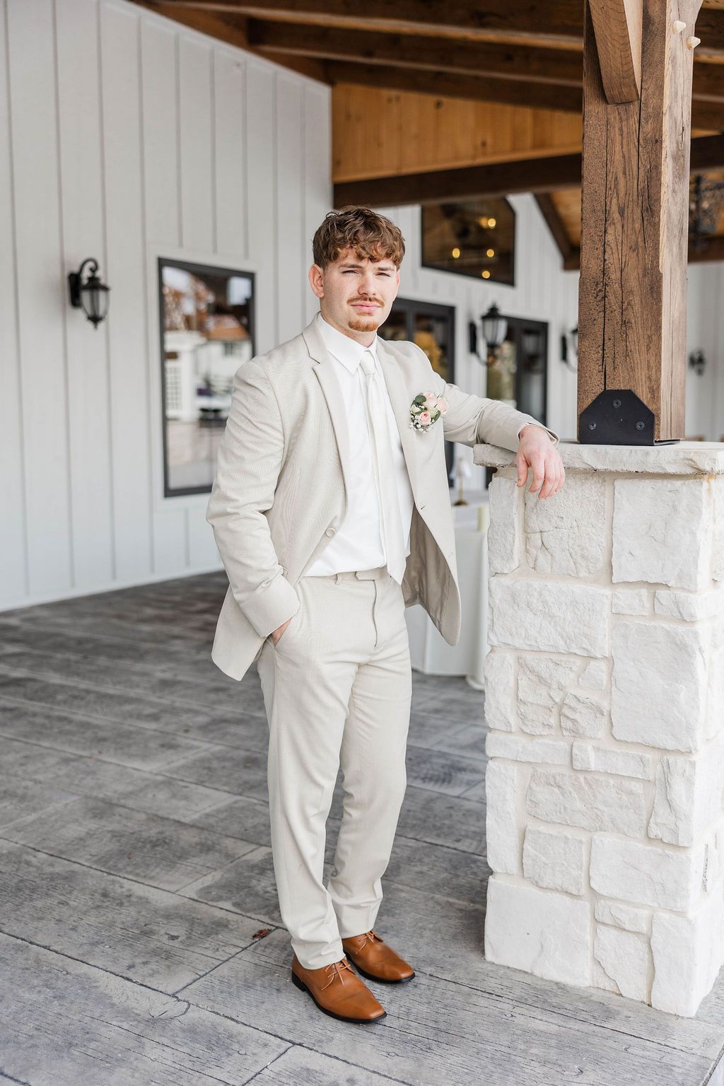 Man in a cream suit leaning on a stone pillar in a rustic porch setting