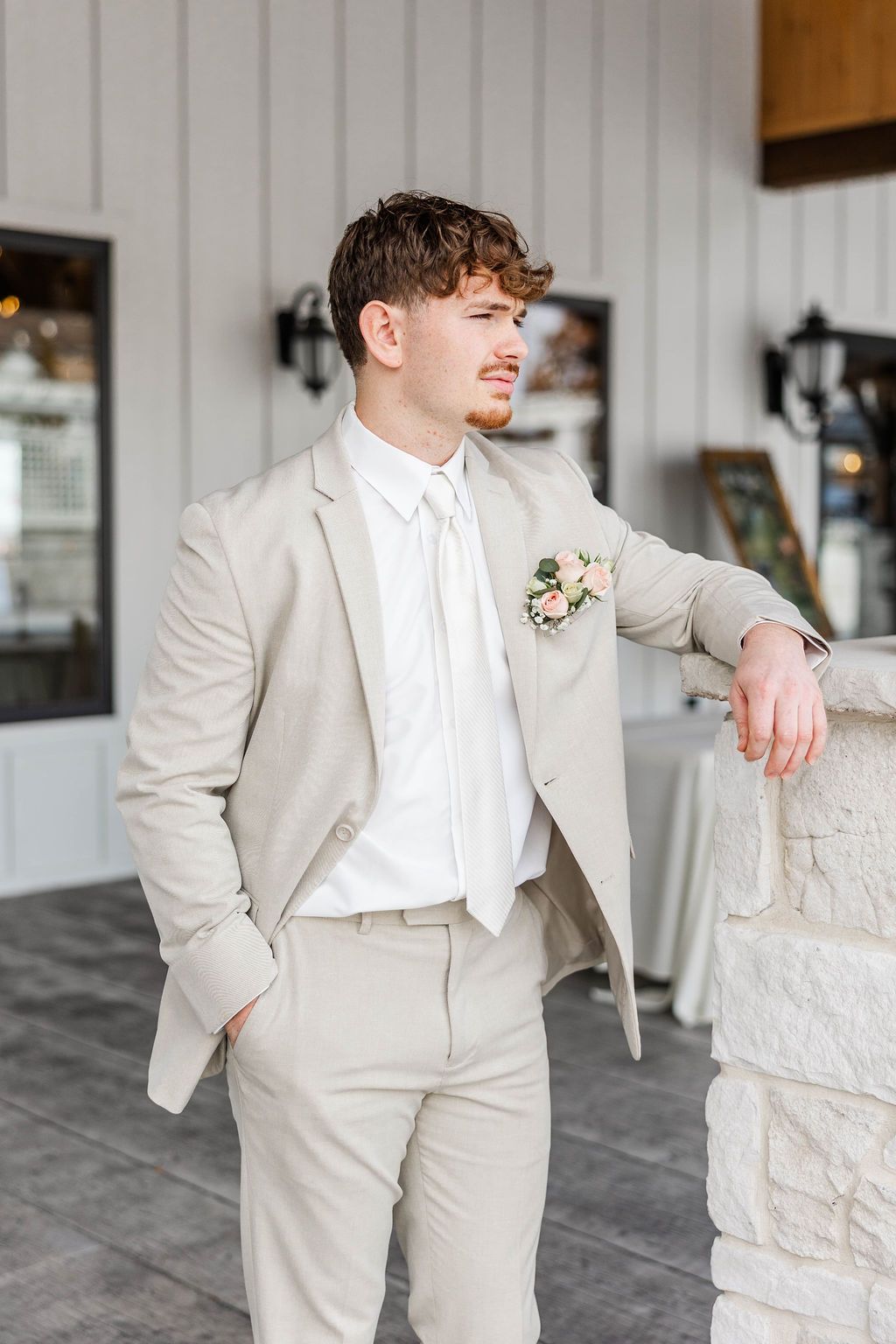 Man in a light beige suit leaning against a stone counter in a bright indoor setting
