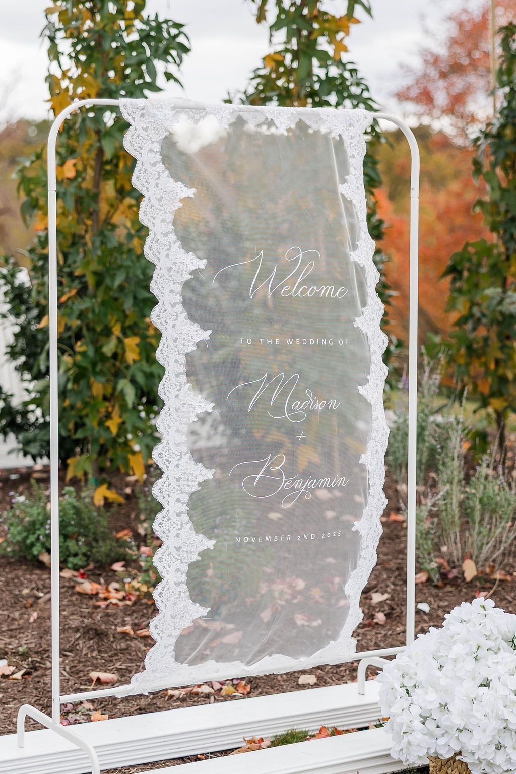 Tall white-framed mesh garden screen with text, flanked by autumn foliage and white flowers