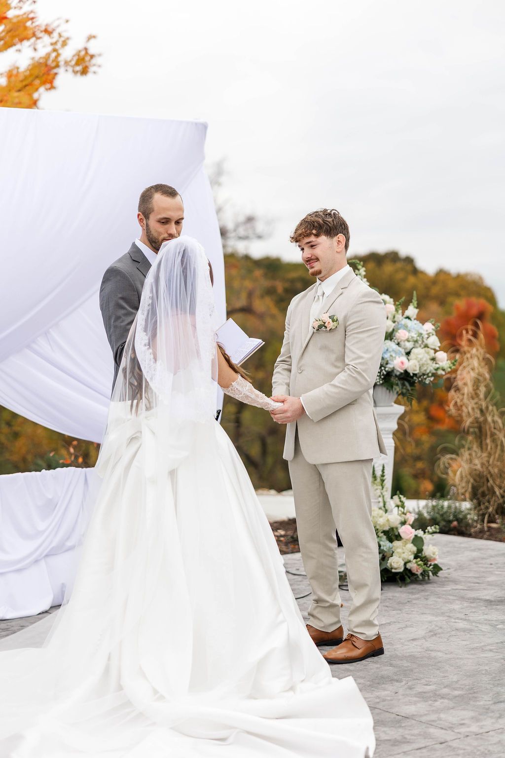 Wedding couple exchanging vows under a white draped arch outdoors in autumn