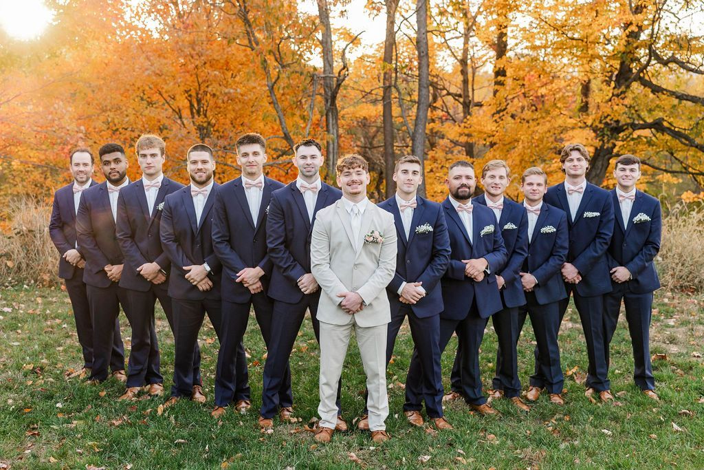 Group of men in suits posing outdoors on grass with autumn trees in the background