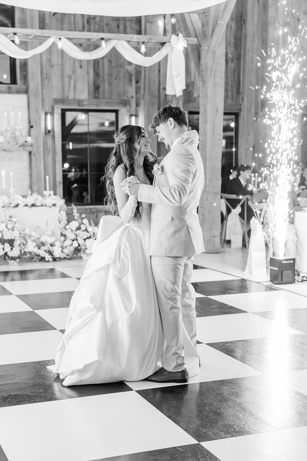 Bride and groom share a dance in a decorated wedding hall with a checkered floor.