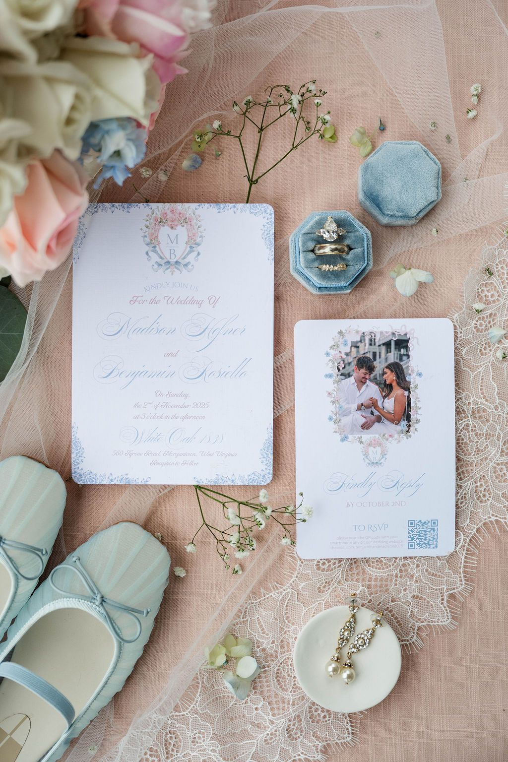 Wedding invitation stationery on blush fabric with flowers, blue lace shoes, and small decorative dishes