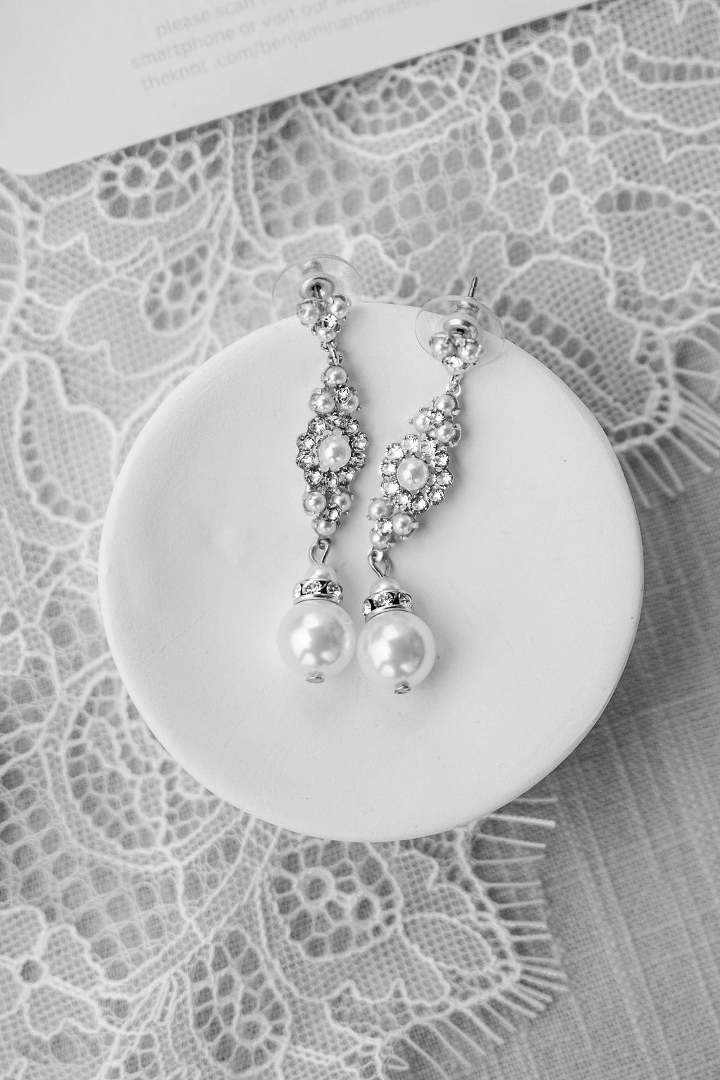 Silver drop earrings with pearls on a round white cushion over lace fabric