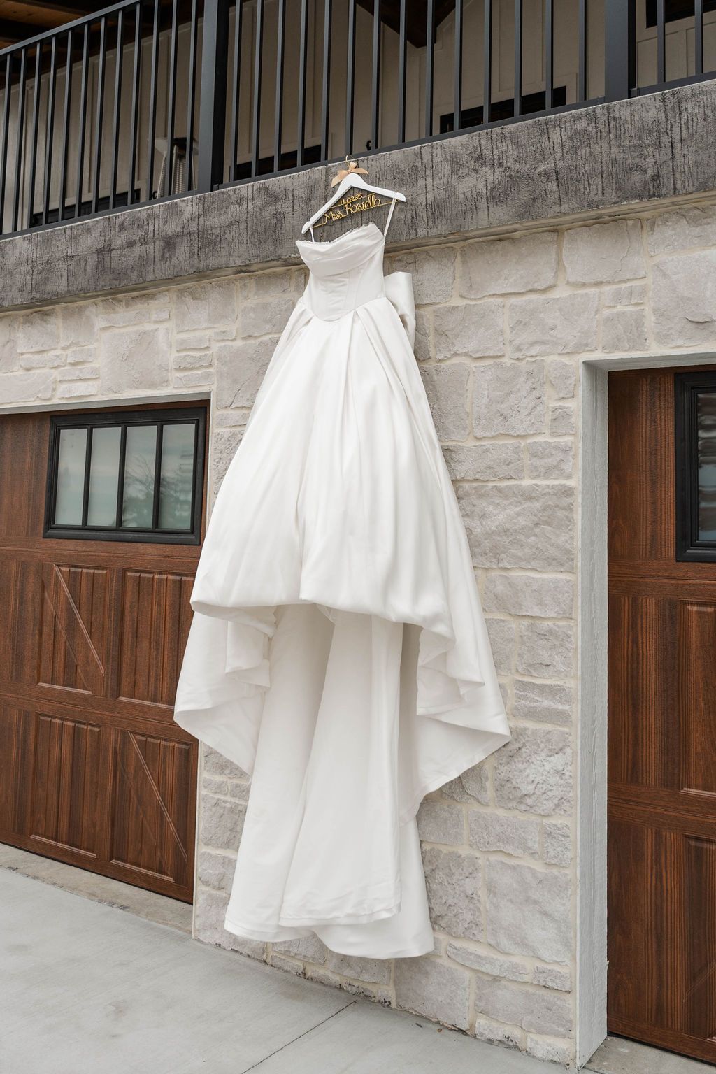 White wedding dress hanging on a stone wall between wooden doors