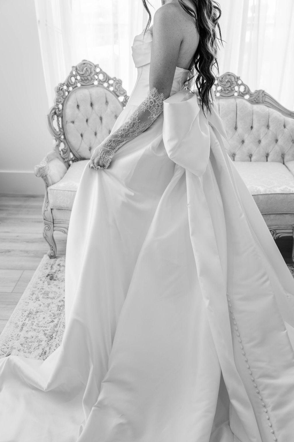 Bridal gown with long train displayed on an ornate sofa in a bright room