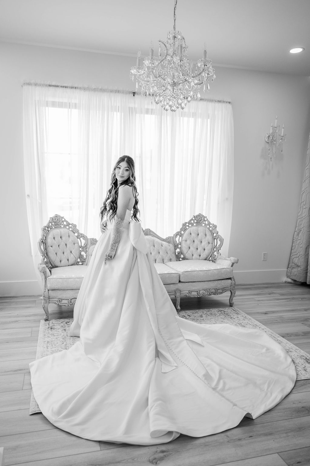 Bridal gown with long train displayed in a bright room with ornate sofa and chandelier
