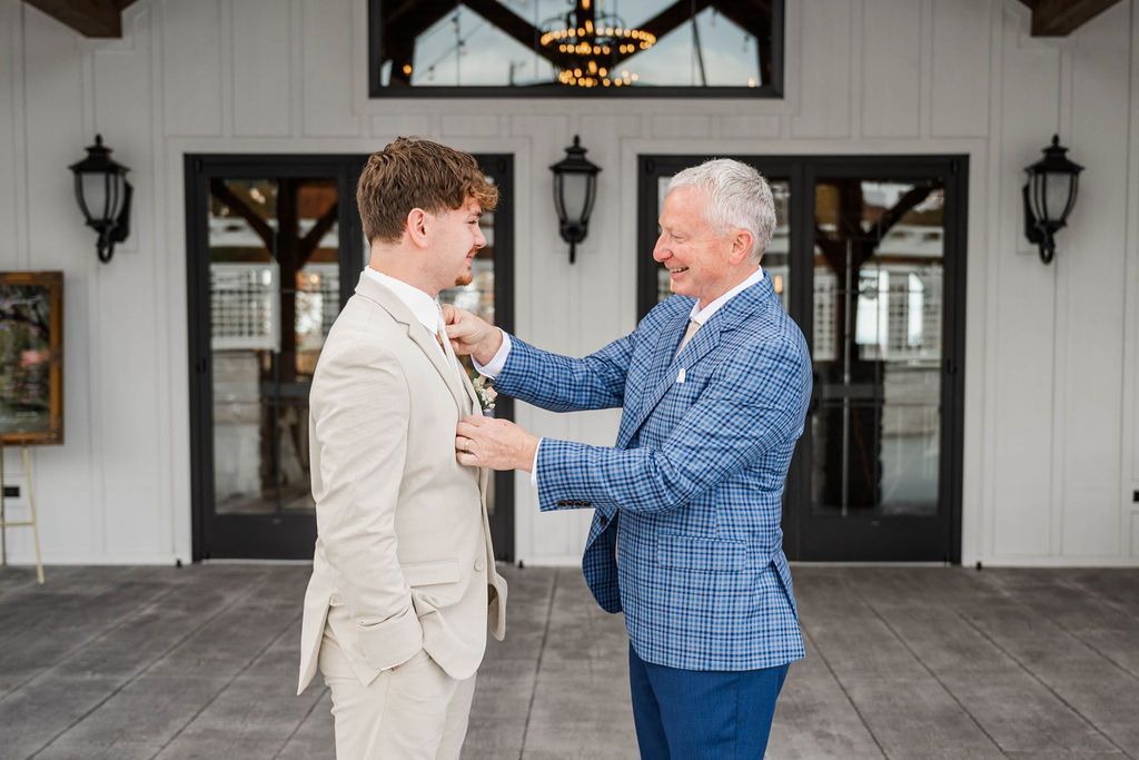 Two men adjusting a suit jacket outside a white building with black doors