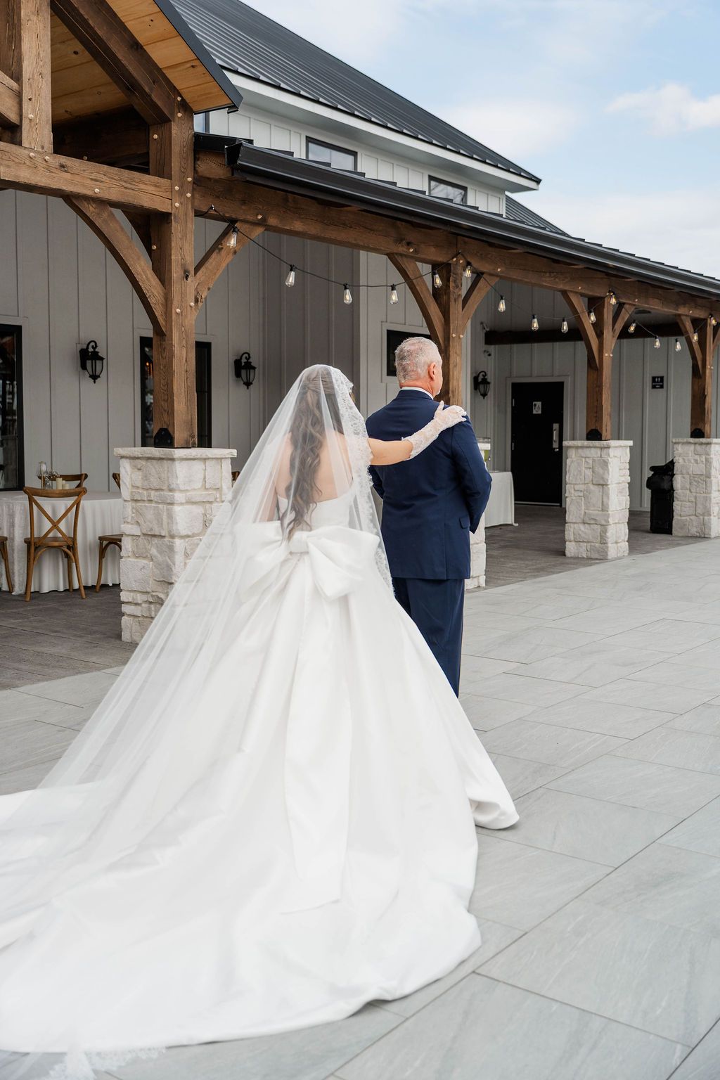 Bride in a white gown and veil walking with a man in a navy suit outside a rustic venue