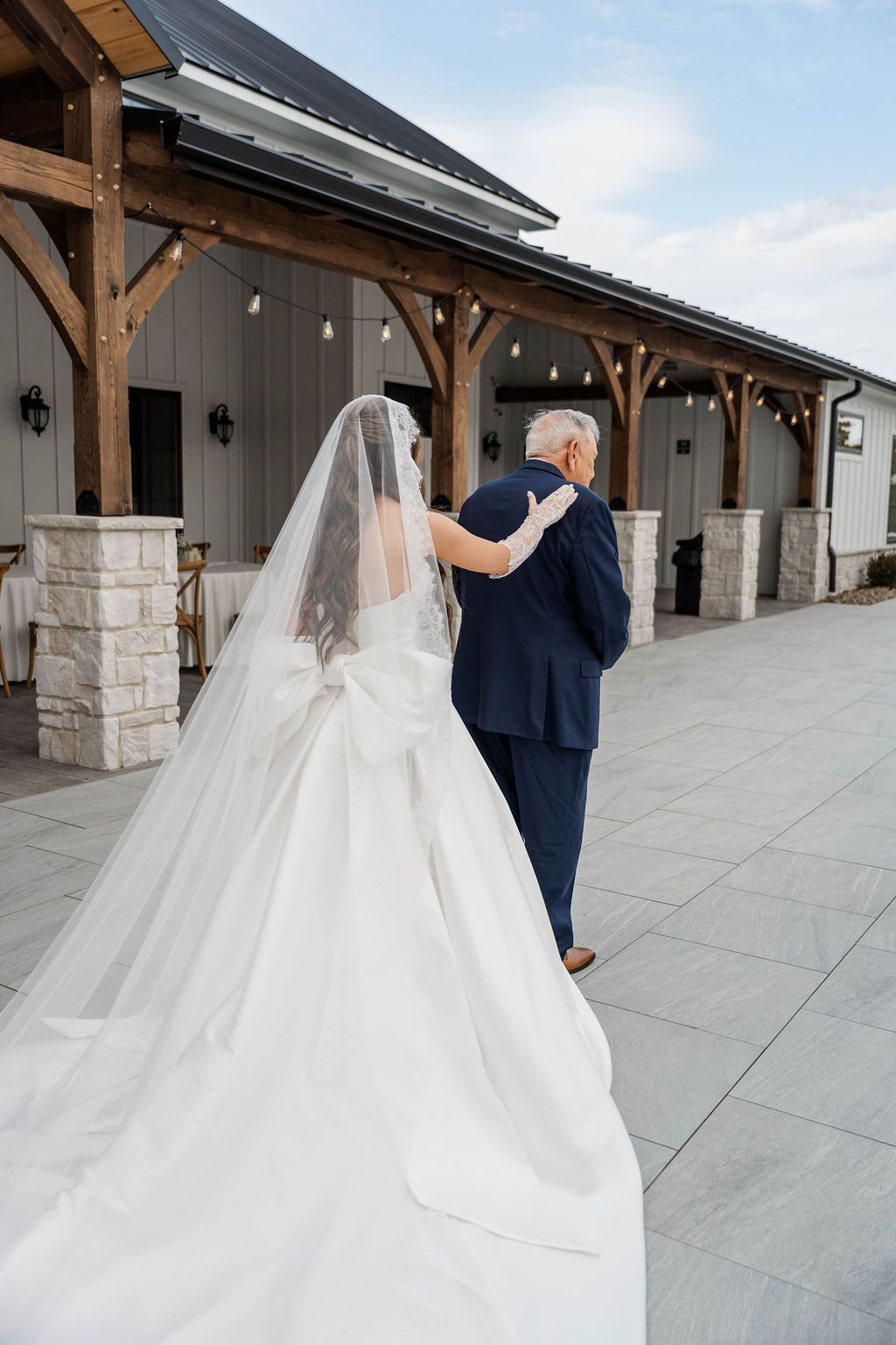 Bride in white gown and veil walking with a guest outside a rustic venue