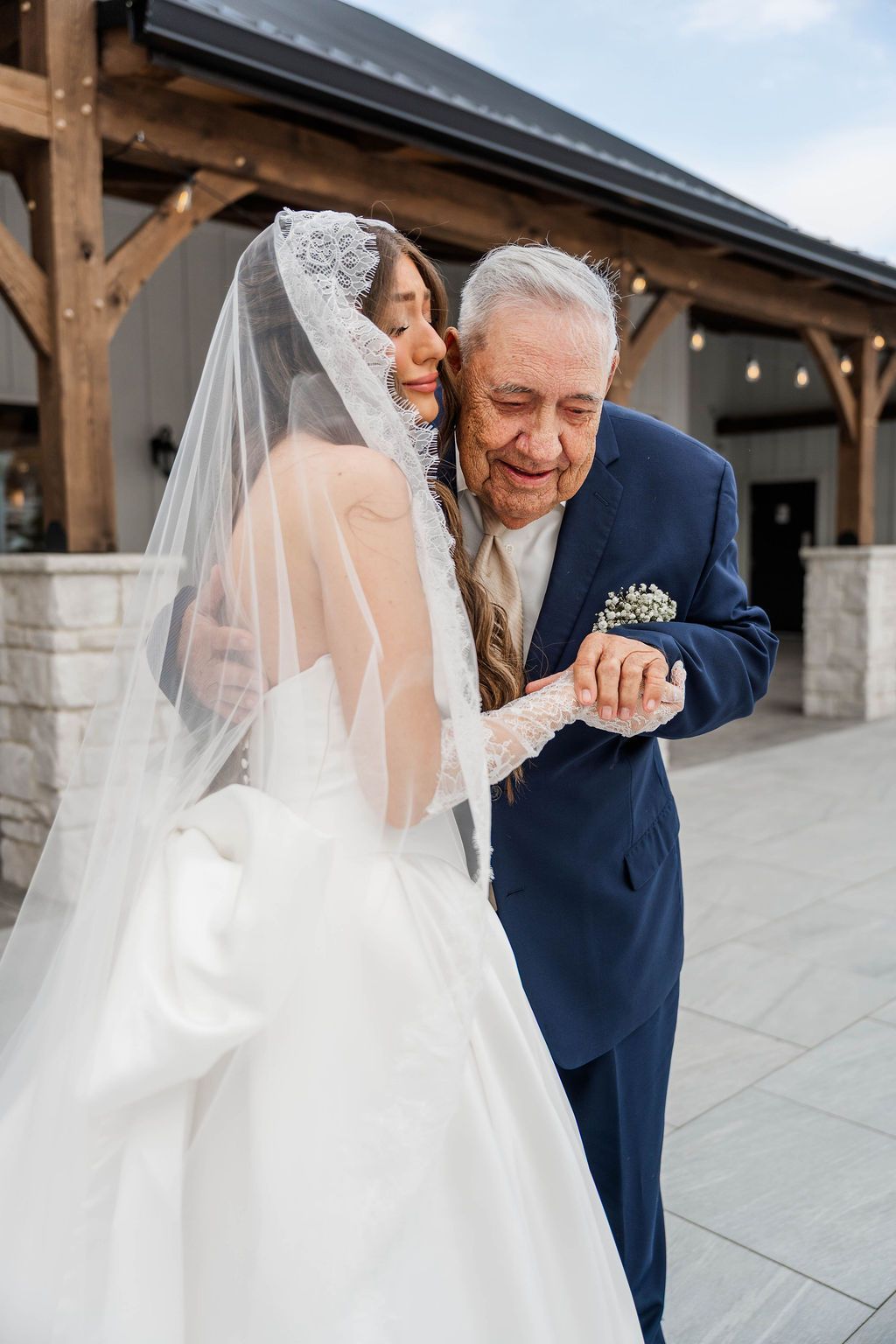 Bride kissing an older man in a blue suit outside a wooden pavilion