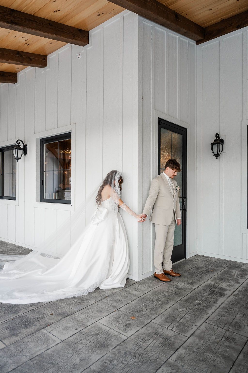 Bride and groom holding hands in a white wooden porch, dressed in wedding attire