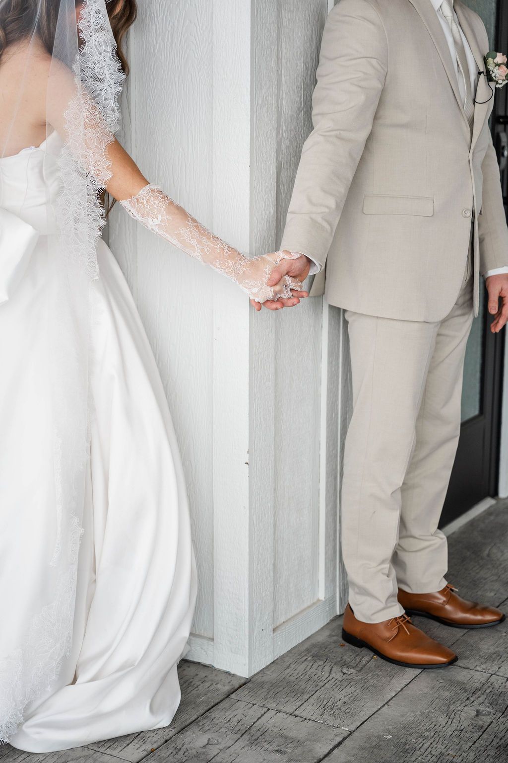 Bride and groom holding hands by a white doorway, in a wedding dress and beige suit