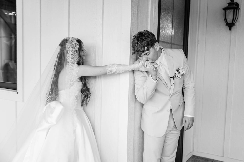 Bride touching groom’s face as he stands by a doorway, in a black-and-white wedding photo