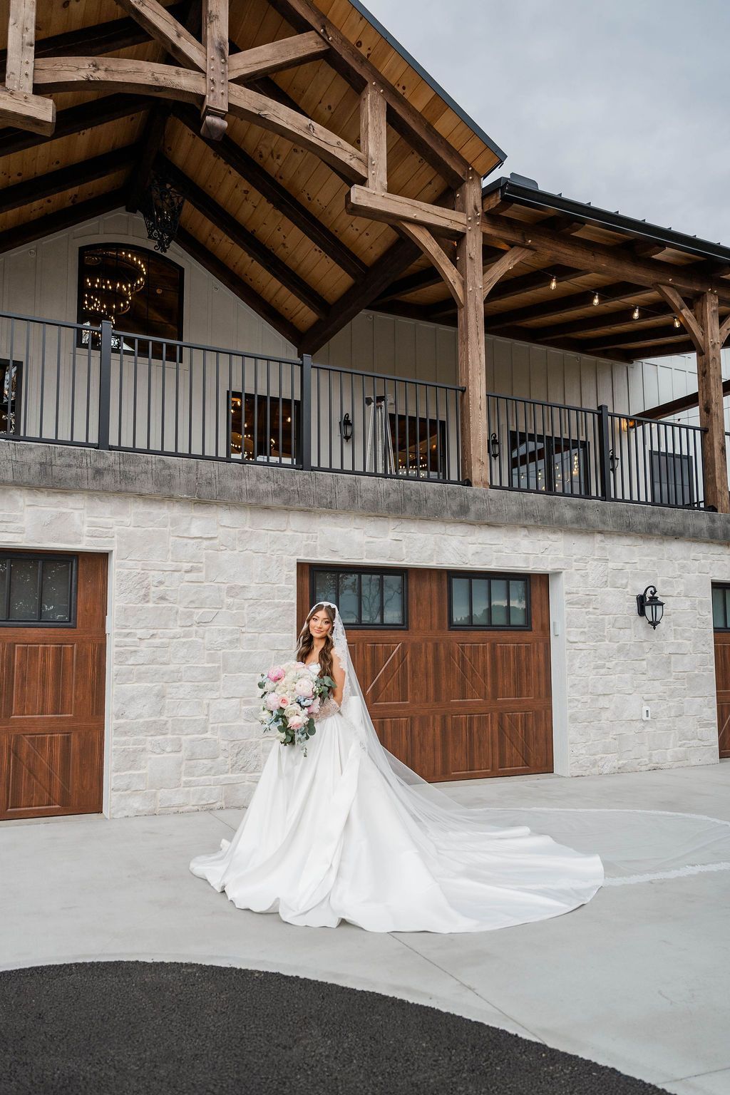 Bride in a white gown holding a bouquet in front of a rustic stone building with a balcony