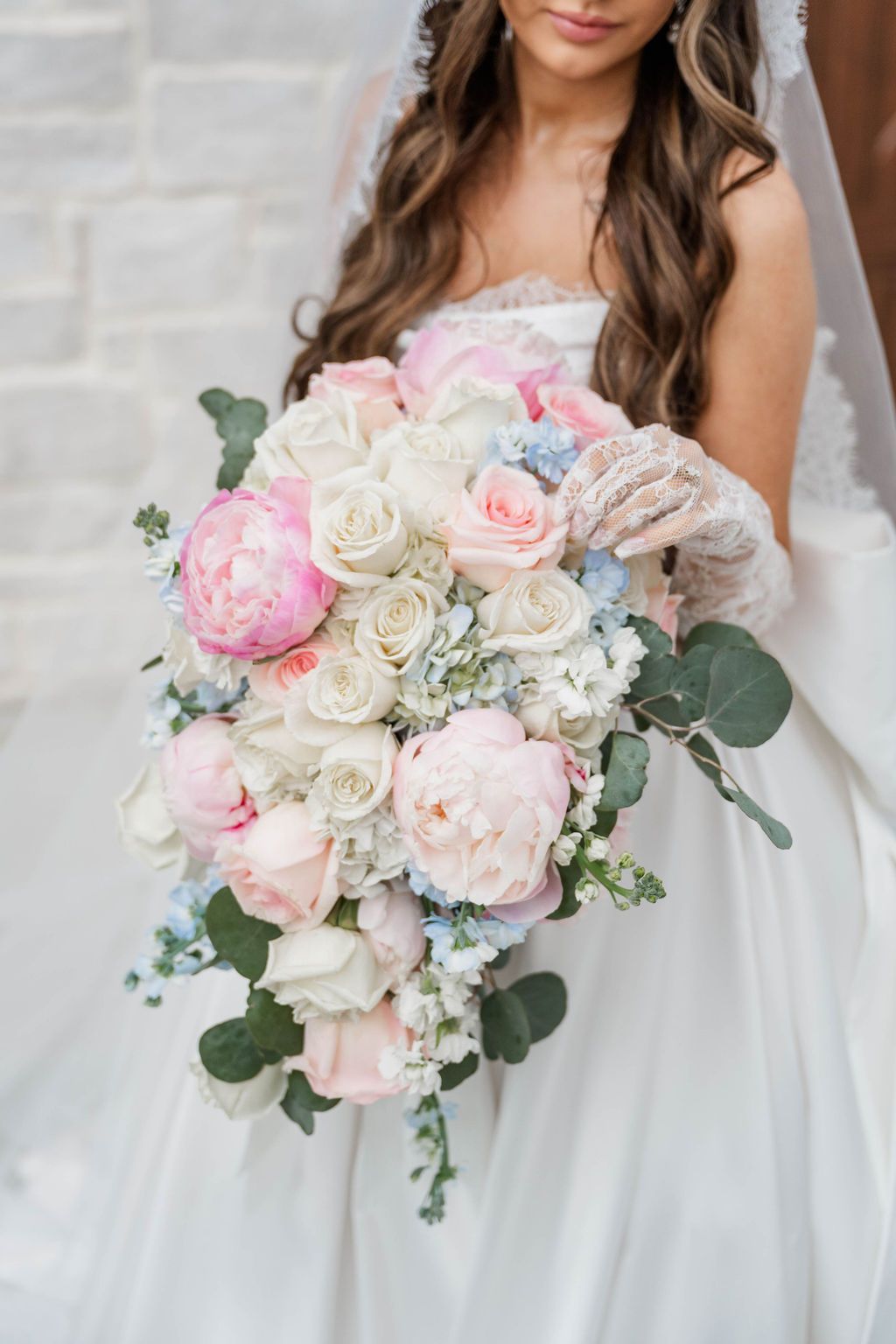 Bride holding a cascading bouquet of white, pink, and green flowers in a white wedding dress