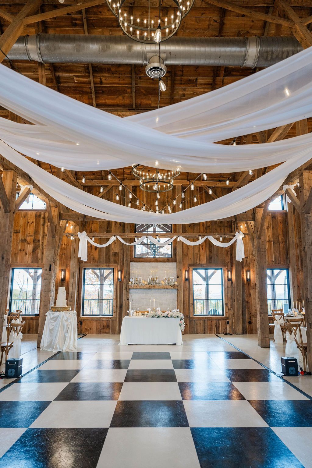 Grand ballroom with white drapes, chandeliers, and black-and-white checkered floor