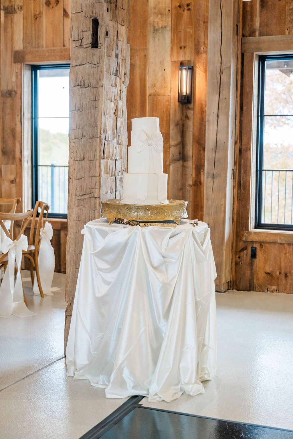 White tiered cake on draped table in rustic wood-paneled room with tall windows