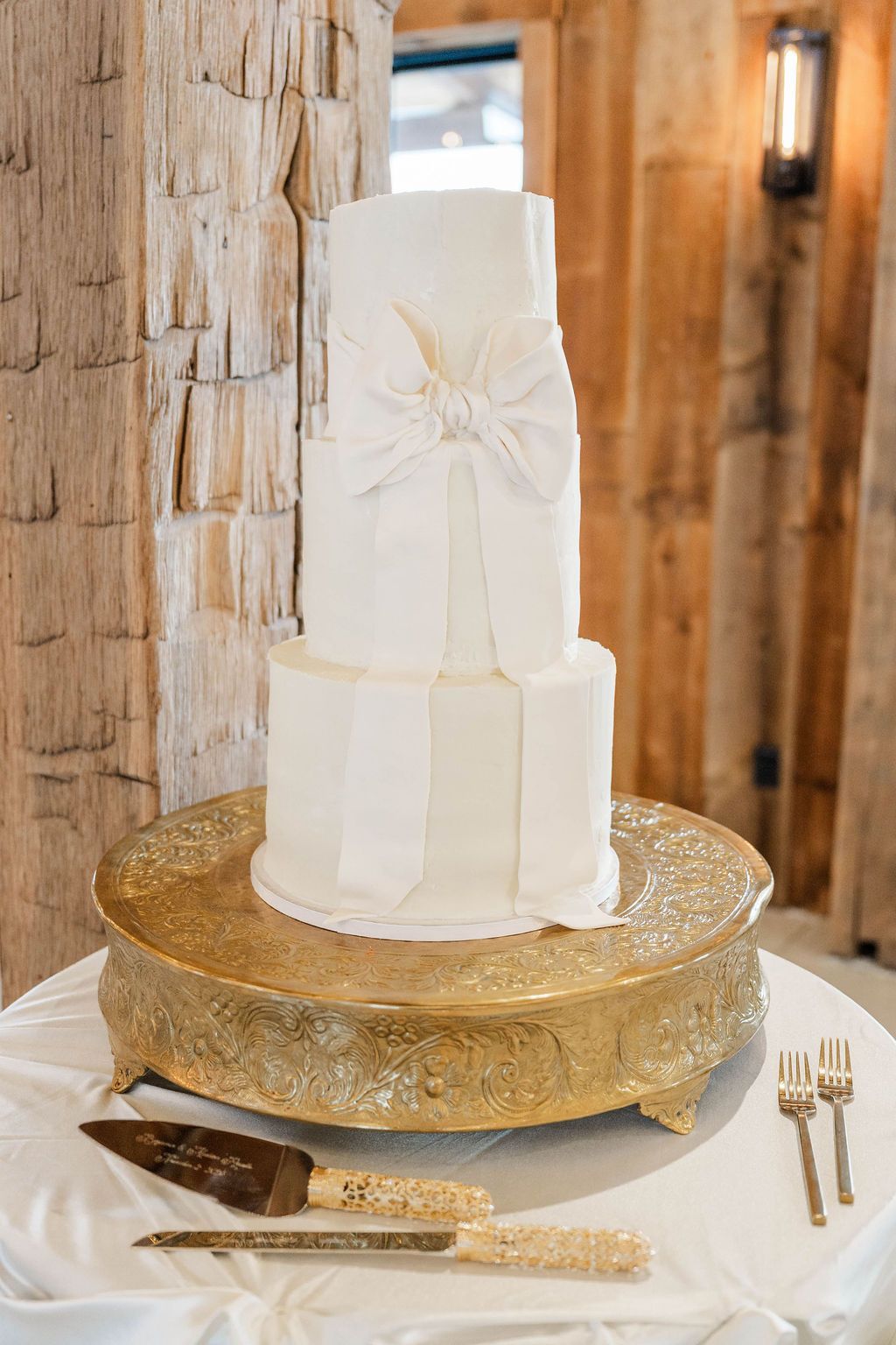 White tiered wedding cake on gold pedestal with glittering decor in a rustic setting