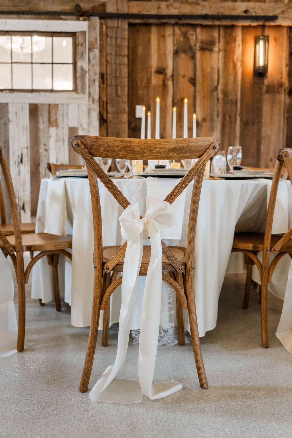 Rustic dining table set with white chairs, candles, and a sheer white ribbon in a wooden room