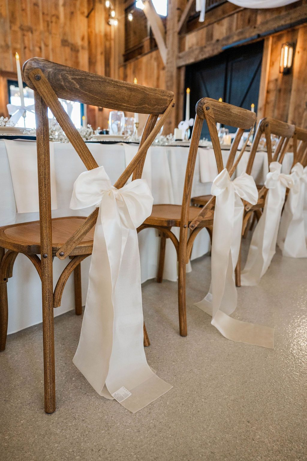 Wooden chairs lined up in a rustic venue, each tied with a large white bow.