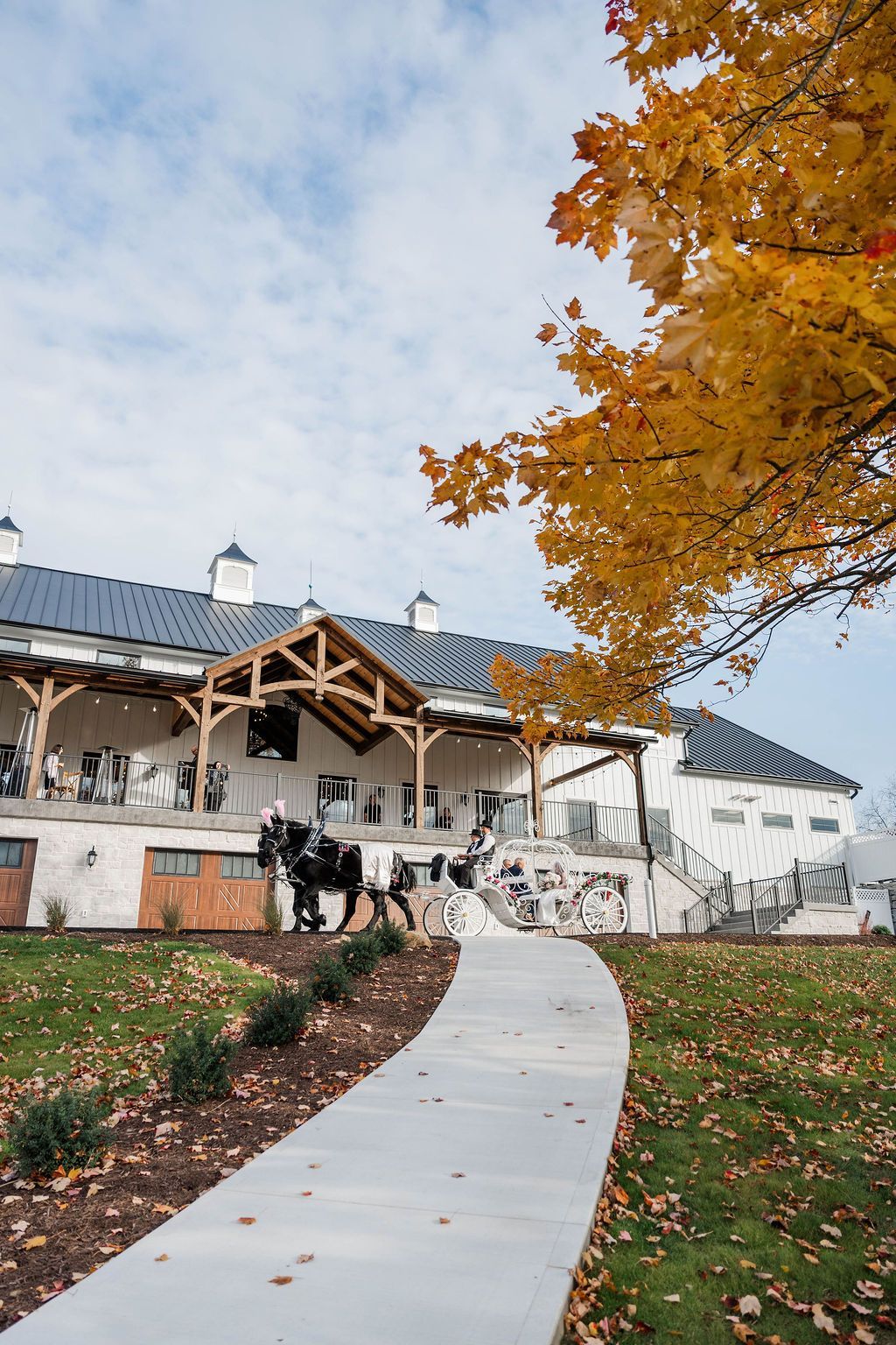Curved walkway leading to a white building with autumn trees and orange leaves, under a cloudy sky