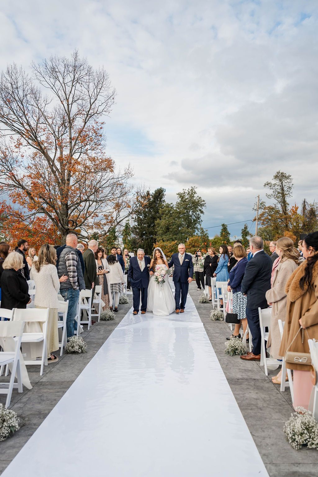 Wedding guests standing beside an outdoor aisle on an overcast day