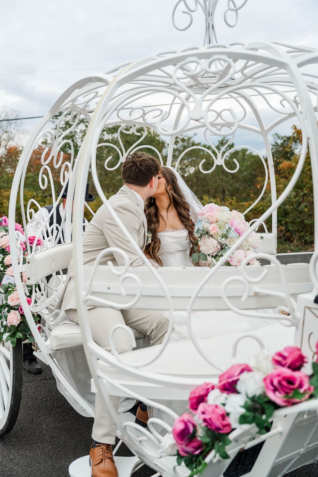 Couple kissing in a white decorative carriage with pink flowers, outdoors in a garden setting