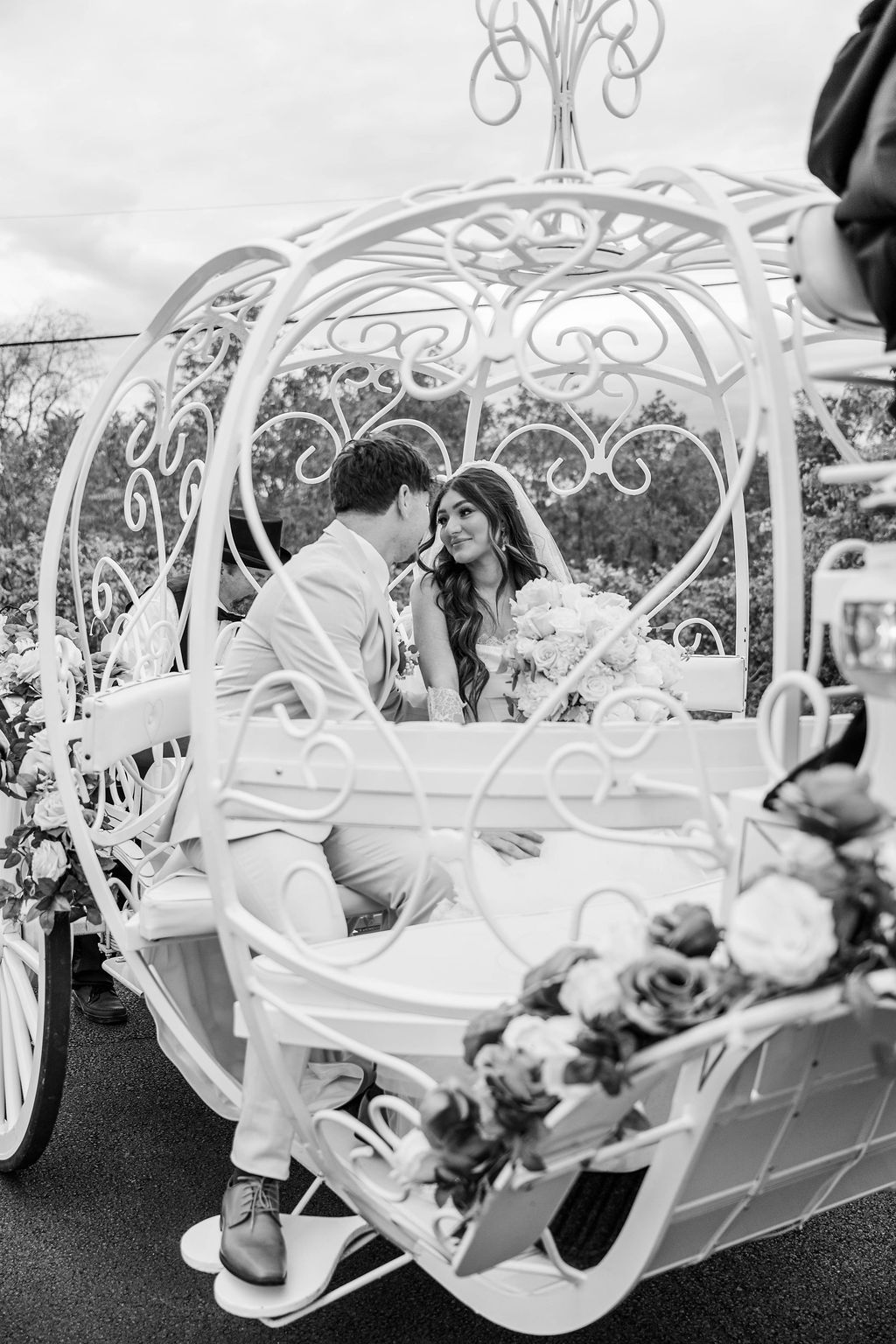 Couple seated in a white decorative carriage, facing each other at an outdoor event