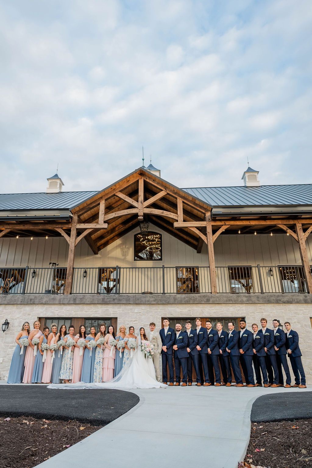 Wedding party posing outside a rustic barn venue under a cloudy sky