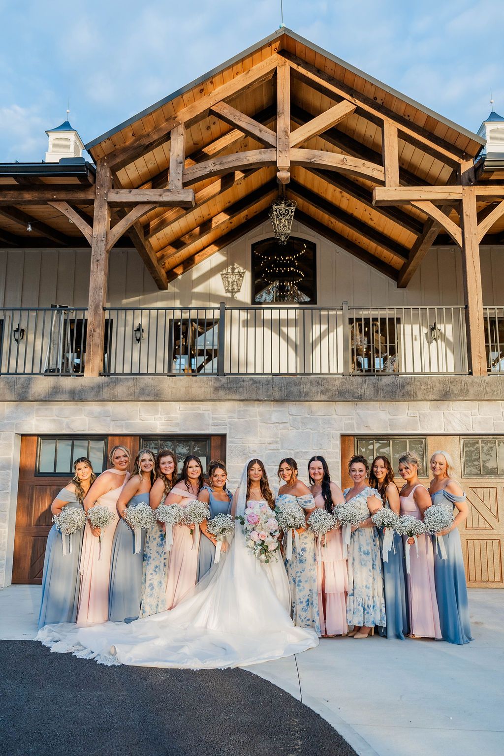 Wedding party posing in front of a rustic lodge, with a bride in a white gown and bridesmaids in pastel dresses.