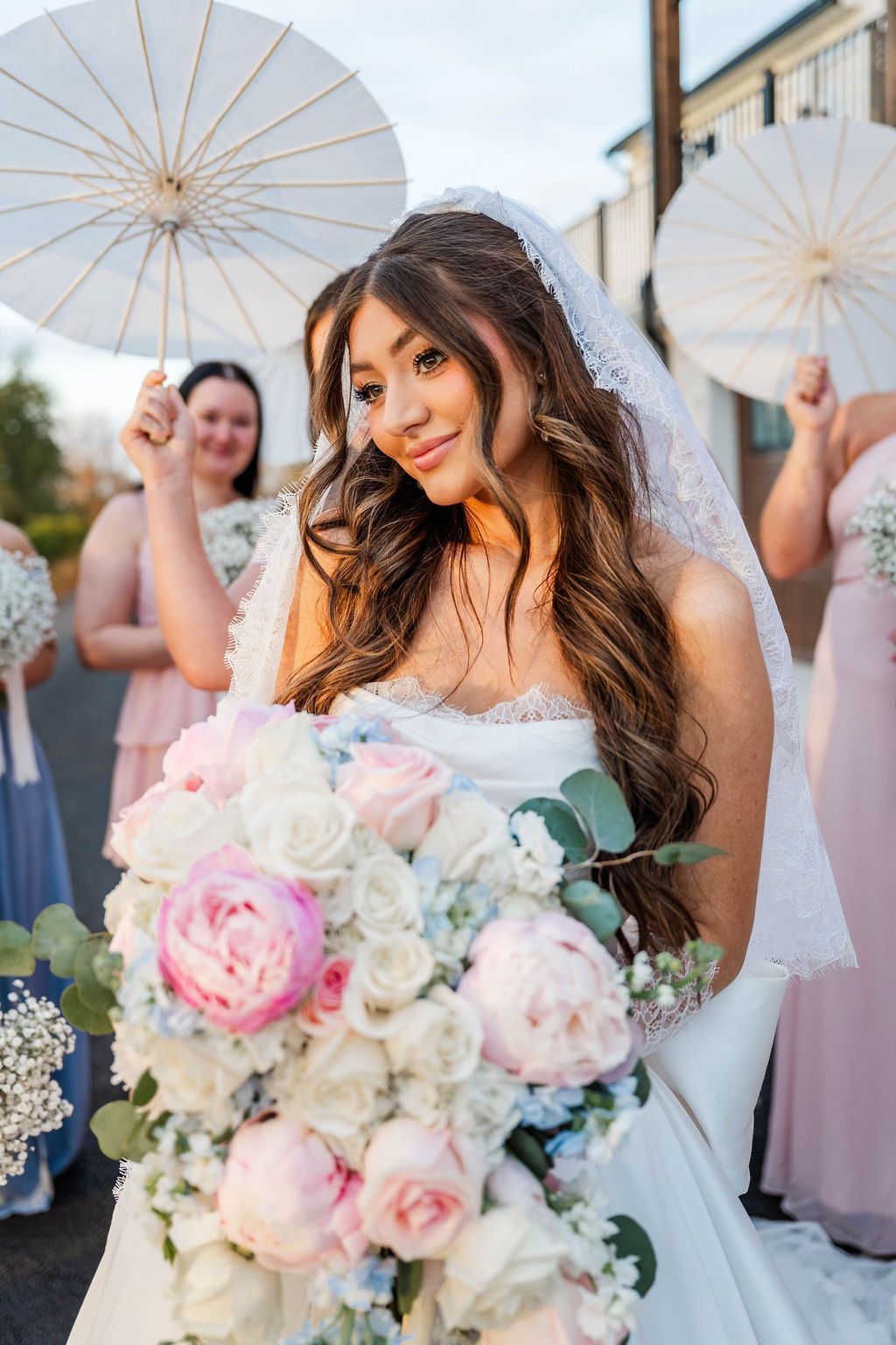 Bride holding pastel bouquet in front of wedding guests with white parasols