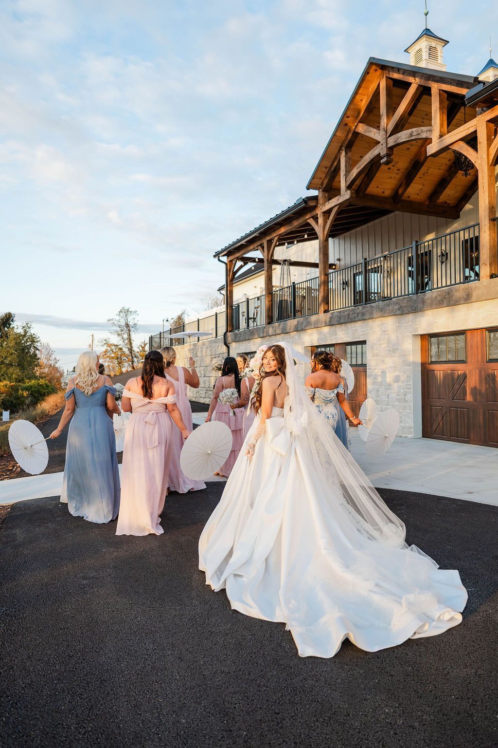 Bridesmaids and a bride in flowing dresses walk outside a rustic lodge at sunset.